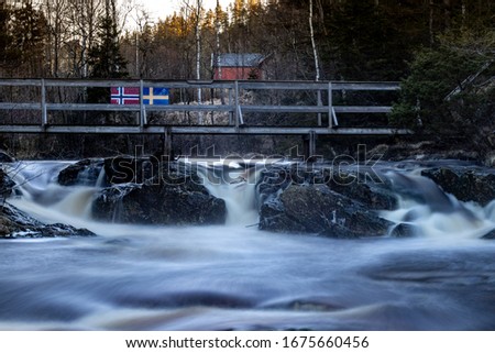 Long exposure photograph of border crossing between Sweden and Norway. It is a wooden pathway over the river Elgofossen.