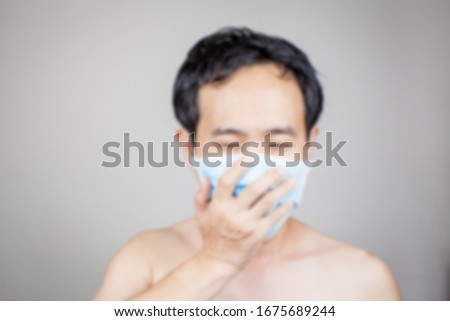 Defocus photo Asian man on stain background sneeze wears medical surgical N95 mask to protect virus COVID 19 and dust pm 2.5pollution that a big problem and spread widely in 2020 cuase health problem 