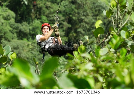 A man gliding through the lush jungle canopy of the Andes in Ecuador on a thrilling zip line adventure over rainforest and water. Royalty-Free Stock Photo #1675701346