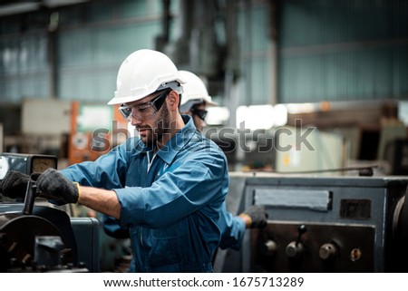 Men industrial engineer wearing a white helmet while standing in a heavy industrial factory behind. The Maintenance looking of working at industrial machinery and check security system in factory.