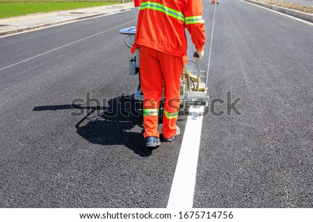 Road workers use hot-melt scribing machines to painting dividing line on asphalt road surface in the city. Royalty-Free Stock Photo #1675714756