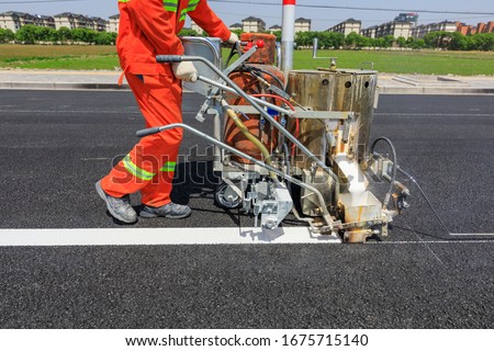 Road workers use hot-melt scribing machines to painting dividing line on asphalt road surface in the city. Royalty-Free Stock Photo #1675715140