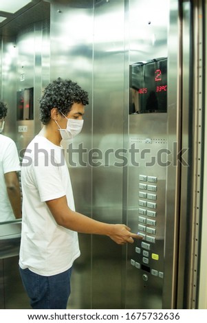22 year old man with protective mask inside an elevator pushing buttons