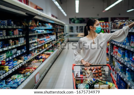 Woman with hygienic mask shopping for supply.Budget buying at a supply store.Emergency to buy list.Shopping for enough food and cleaning products.Preparation for a pandemic quarantine due to covid-19