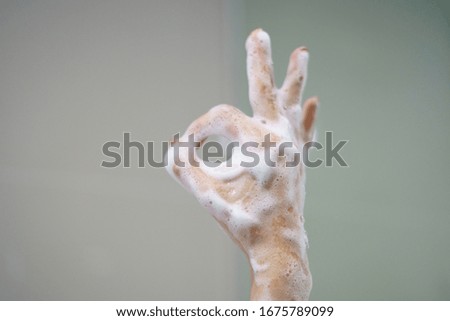 Hand with soft foam bubble from soap is showing ok sign.