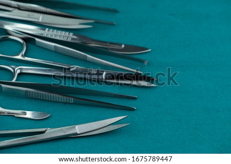 Basic surgical instrument scalpel forceps tweezers scissors spread on surgical green drape fabric