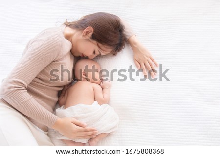 Asian beautiful mom motherhood lie down nursing, kissing newborn baby infant toddler, gently hold together on chest with love, infant sleep comfortable with safe and protection by mother taking care