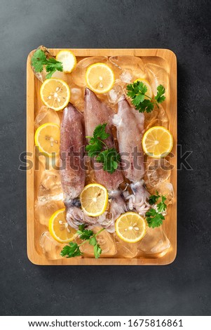 A plate of ice cubes with fresh tubules of squid and lemon slices on a black background	

