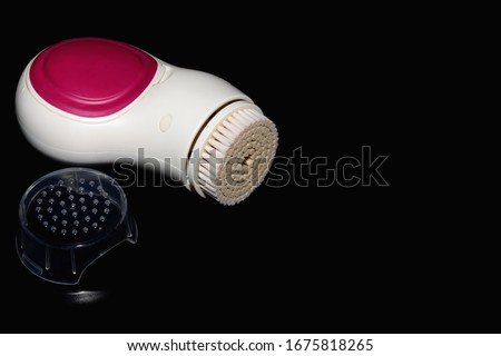 Electric facial cleansing brush isolated on black background.