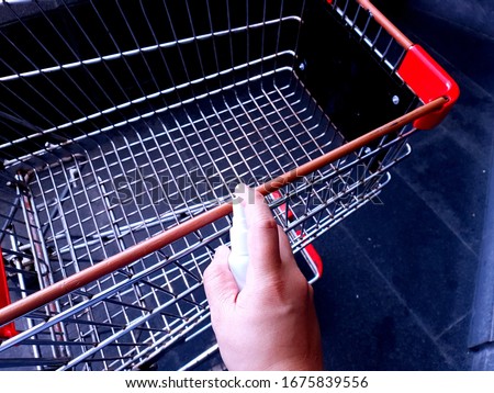 Cleaning shopping cart with alcohol spray. Corona Virus or bacteria infected protection from touch public object. Customer self-protection in public place concept. Royalty-Free Stock Photo #1675839556