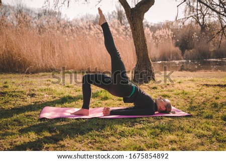 Young healthy attractive woman practicing yoga outdoor standing in One legged Wheel exercise, Bridge pose, working out, wearing sportswear