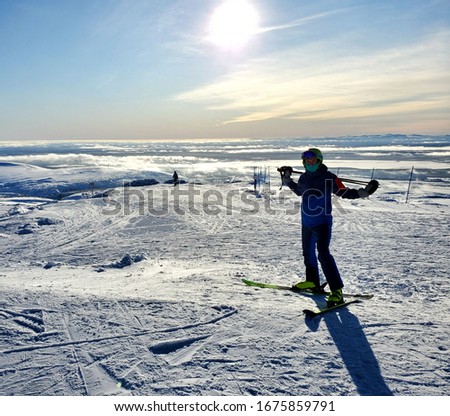 young, slender young man in sportswear, helmet, skiing, one stands on a snowy, ski slope in the early sunny morning.