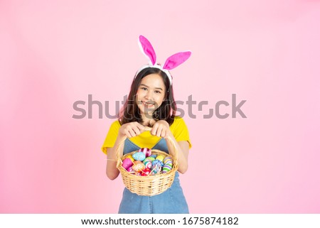 Half length studio shot of asian beauty happy young woman wearing bunny ears and holding colorful Easter egg in wood basket with lovely smile and colorful decor costume isolated on pastel backgrounds.