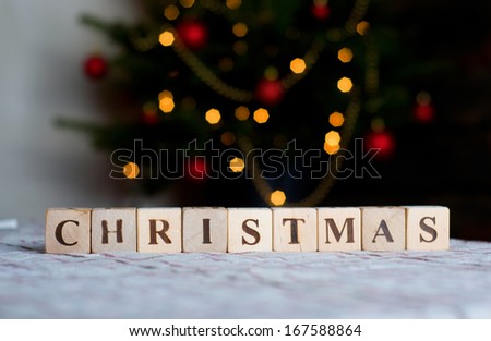 christmas spelled out in wooden blocks with christmas tree background