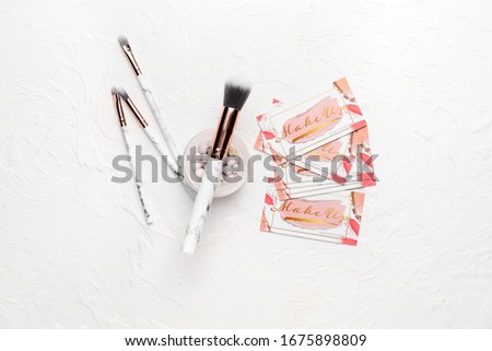 Decorative cosmetics with business cards of makeup artist on white background
