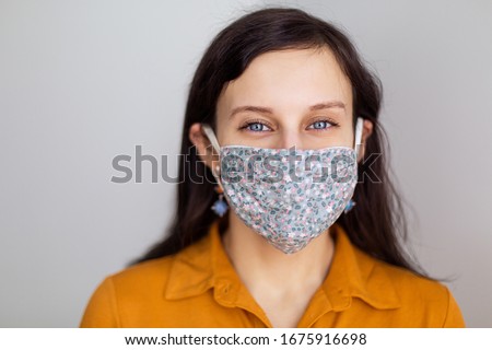 beautiful European girl with blue eyes in a handmade mask from the coronavirus. Design work protecting the security of disinfection of quarantine. Lack face cover. Pandemic houses white background Royalty-Free Stock Photo #1675916698