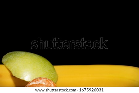 Banana, orange mandarin and cut apple on a black background