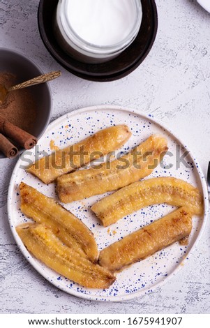 Top view of kitchen table with fried bananas on a plate and bowl with cinnamon and coconut butter Royalty-Free Stock Photo #1675941907