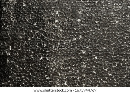 The texture of the foam ball painted black. White foam is visible through the paint