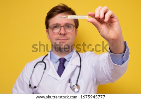 Caucasian mature doctor with stethoscope holding a medical thermometer smiling. His patient is recovered. Temperature, fever, flu or ill diagnostic equipment. Hospital tool or instrument.