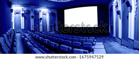 Cinema theater screen in front of seat rows in movie theater showing white screen projected from cinematograph. The cinema theater is decorated in classical style for luxury feeling of movie watching. Royalty-Free Stock Photo #1675947529