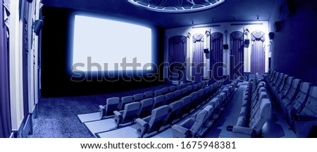 Cinema theater screen in front of seat rows in movie theater showing white screen projected from cinematograph. The cinema theater is decorated in classical style for luxury feeling of movie watching. Royalty-Free Stock Photo #1675948381