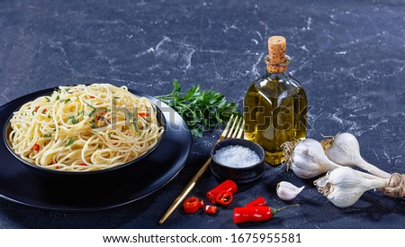 Pasta Aglio, Olio e Peperoncino, italian spaghetti with garlic, chili pepper and olive oil in a black bowl with golden fork and ingredients on a concrete table, close-up, free space Royalty-Free Stock Photo #1675955581