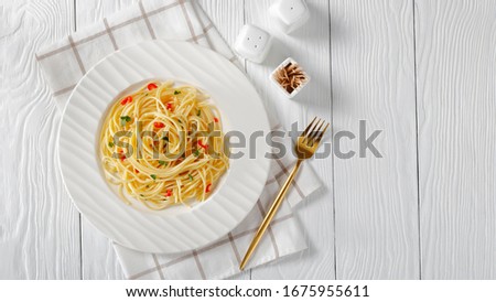 Pasta Aglio, Olio e Peperoncino, italian spaghetti with garlic, chili pepper and olive oil on a white plate with golden fork and salt shaker on a wooden table, close-up, free space, flat lay Royalty-Free Stock Photo #1675955611