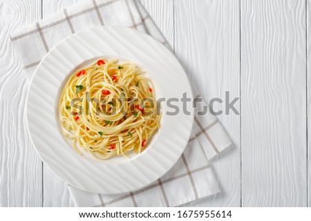 Pasta Aglio, Olio e Peperoncino, italian spaghetti with garlic, chili pepper and olive oil on a white plate on a wooden table, close-up, free space, flat lay, horizontal view from above Royalty-Free Stock Photo #1675955614