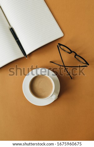 Modern home office desk workspace with notebook, cup of coffee, glasses on ginger background. Flat lay, top view work, business concept.