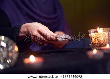 Fortuneteller female divines on cards sitting at table with burning candles