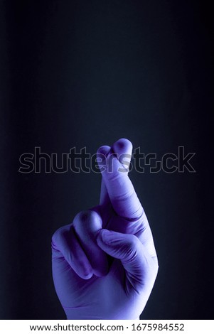 Sign for hope is showed by right man hand in a purple medical glove on a black background. The good luck symbol.