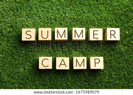 Phrase SUMMER CAMP made with cubes on green grass, flat lay