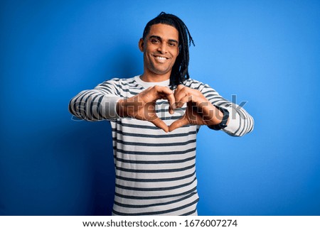 Young handsome african american afro man with dreadlocks wearing casual striped sweater smiling in love doing heart symbol shape with hands. Romantic concept.