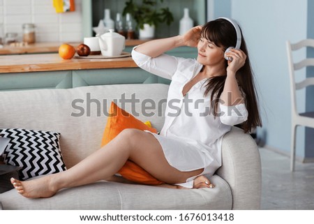A young beautiful girl is enjoying music while sitting on a sofa among bright pillows. Rest, relaxation, lifestyle
