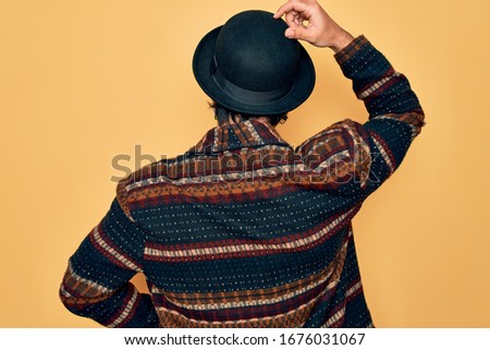 Young handsome hispanic bohemian man wearing hippie style and boho hat Backwards thinking about doubt with hand on head