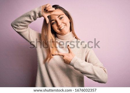 Beautiful blonde woman with blue eyes wearing turtleneck sweater over pink background smiling making frame with hands and fingers with happy face. Creativity and photography concept.