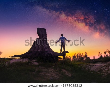 Silhouette man stane alone on tree stump at night sky background with Milky way on the sky.
