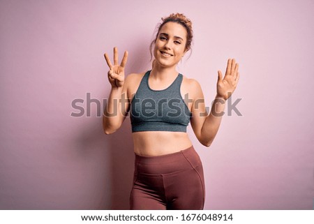 Young beautiful blonde sportswoman doing sport wearing sportswear over pink background showing and pointing up with fingers number eight while smiling confident and happy.
