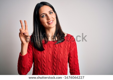 Young brunette woman with blue eyes wearing casual sweater over isolated white background smiling looking to the camera showing fingers doing victory sign. Number two.
