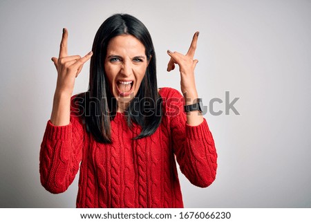 Young brunette woman with blue eyes wearing casual sweater over isolated white background shouting with crazy expression doing rock symbol with hands up. Music star. Heavy music concept.