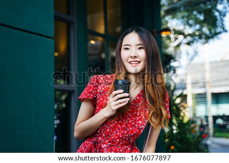 Cheerful Young asian woman on red dress holding a cup of coffee at cafe outdoors.
