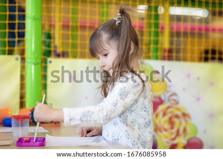 a little girl draws with a brush on paper . a child learns to draw in kindergarten