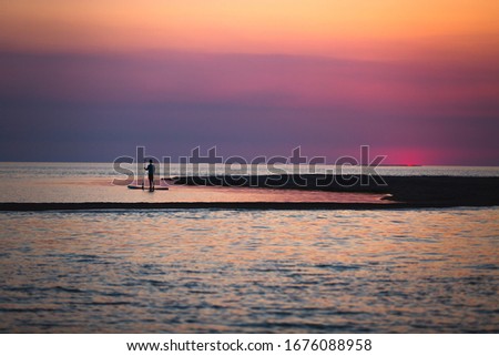 Person silhouette stand up paddle boarding at dusk on a flat quiet sea on sunset