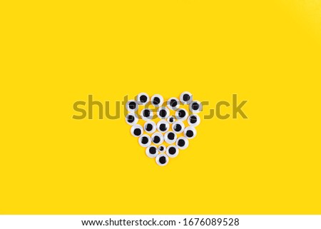 Heart shape made of Googly plastic eyes on yellow background. Used for imitation of eyeballs for handcraft toys and dolls and others creativity. Flat lay.