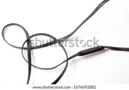 Black headphones cable flat wire layed out on a white background shot professionally in a studio tangled up with a button control on the headset with no branding on for commerce commercial use 