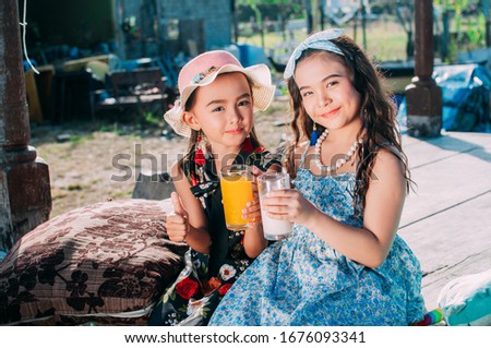 Cute little girl is drinking milk and orange juice in the countryside