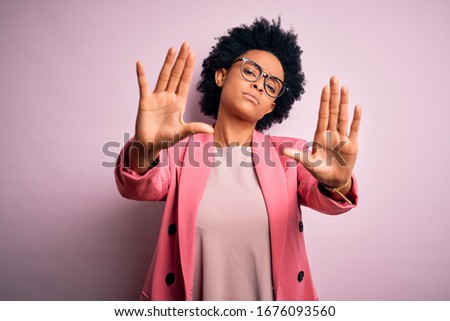 Young beautiful African American afro businesswoman with curly hair wearing pink jacket doing frame using hands palms and fingers, camera perspective