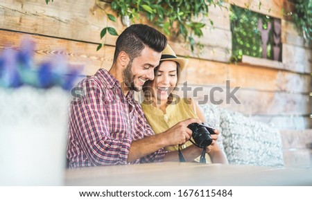 Happy couple checking photos on mirrorless camera during holidays - Young people having fun during travel vacation shooting photos - Influencer and content creators concept - Focus on male face