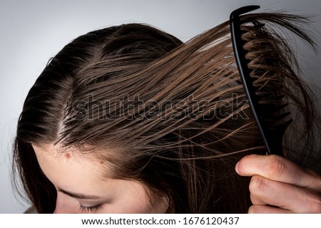 Young woman combing dirty greasy hair on gray background.  Royalty-Free Stock Photo #1676120437